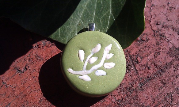 Small round autumnal silhouette series pendant - ivory branches and leaves inlaid into green base with silver bail, against red-brick and ivy